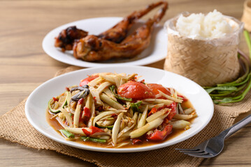 Spicy papaya salad (Som Tum) eating with sticky rice and grilled chicken wing on wooden table, Local Thai food