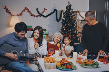 Multi-Generation Family Celebrate Christmas At Home Wearing Santa Hats And Antlers Opening Presents