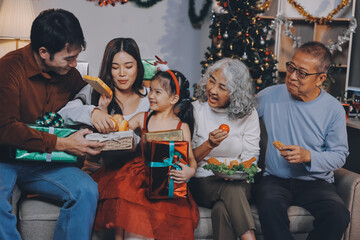 Portrait of Asian family exchanging presents during christmas at home. Attractive happy people holding gift box, celebrate holiday thanksgiving, xmas eve tradition in living room in house together.