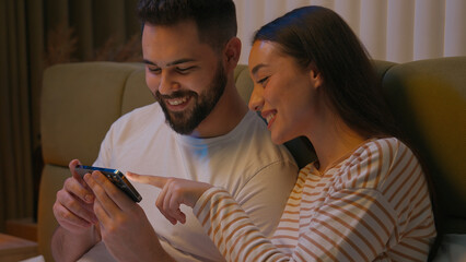 Caucasian couple man woman boyfriend girlfriend together bed bedroom mobile phone smartphone gadget laughing smiling watching funny video technology enjoy humor browsing female male sweetheart spouses