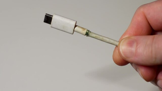 Broken charging cable, close-up. Hand holding frayed charging cable type C