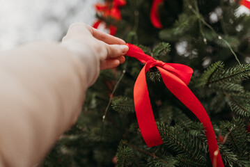 Woman's hands against the Christmas tree with festive decoration with red bows