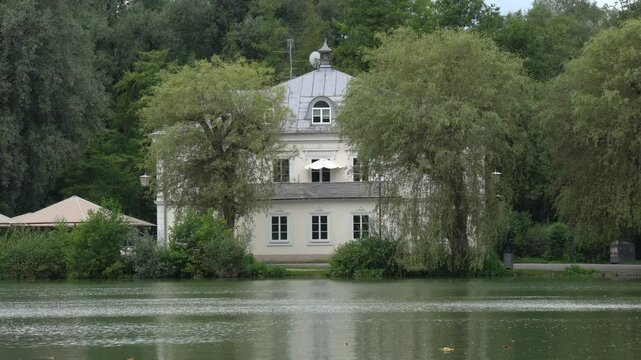 Elegant historic building surrounded by trees, reflecting on the calm waters of Leopoldskroner Weiher lake, Salzburg, Austria.