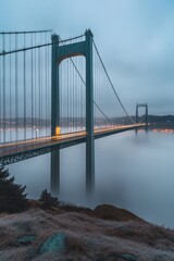 Suspension bridge over foggy water at dawn.