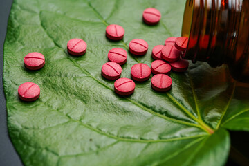 Red herbal capsule pill with herbs and natural green betel leaf background
