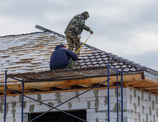 Two men are working on a roof, one of them is using a tape measure