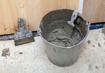 A bucket of cement is sitting on the ground next to a trowel