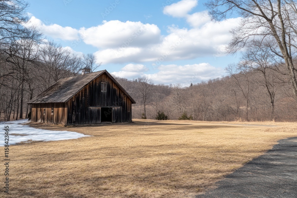 Poster rustic wooden barn in a field, partially snow-covered, with hills and trees in the background under 