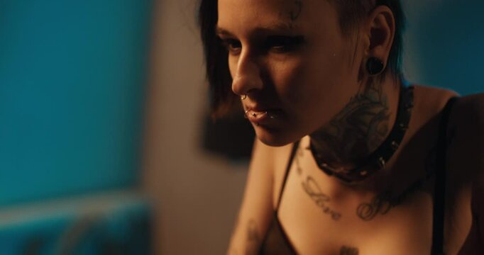 Possessed woman with black eyes and tattoos on face and body, portrait shot. Attractive lady with short hairstyle flirting and seducing, female sexuality and alternative style of woman appearance