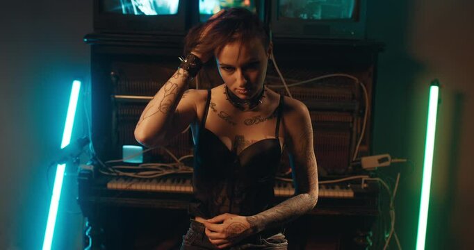 Strange tattooed woman looking at camera aggressively and dangerously, portrait. Female sexuality and sensuality, drug addicted lady in dark room with old furniture, emotional female person in dark