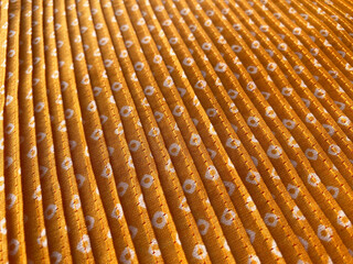 A close-up view of intricate white bandhani block prints adorning mustard silk fabric, enhanced by...