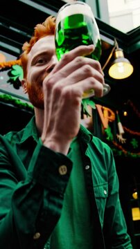 Smiling red-haired man holding green beer outdoors and doing cheers jesture