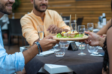 Hands passing a shared platter with gourmet appetizers during elegant dinner