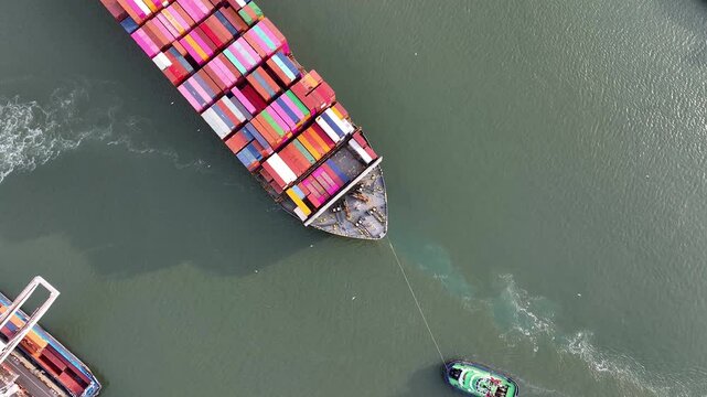 Drone shot of a large container ship entering or leaving the modern industrial container port of Rotterdam with containers on top. This is a port for import and export cargo, part of the shipping dock