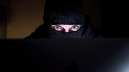 A man dressed in black approaches a computer, his eyes visible and focused, within a dark setting, creating a tense atmosphere of cyber attack, hacking