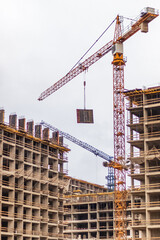 Construction cranes lifting materials at a building site under a gray sky for urban infrastructure