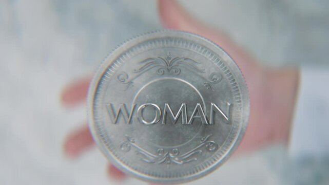A hand flips a coin marked Man and Woman, spinning toward the camera in slow motion