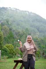 Young Indonesian woman wearing hijab enjoying the calming natural atmosphere while enjoying a cup...