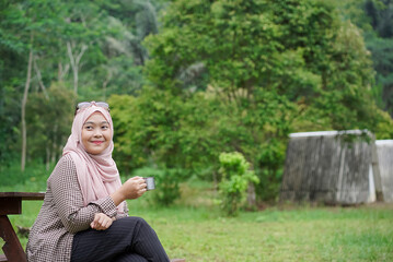Young Indonesian woman wearing hijab enjoying the calming natural atmosphere while enjoying a cup...