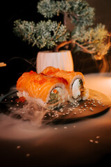 Sushi on a board on a black background. Philadelphia set. Rolls in smoke. Japanese cuisine concept