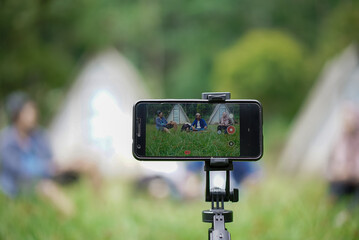 Portrait of a cellphone recording a video of young Indonesian men and women while camping in a forest cabin, travel concept.
