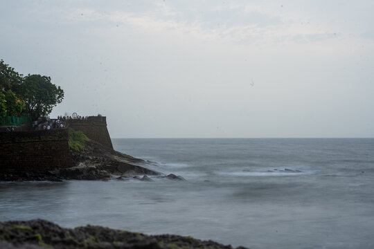 Tourists enjoying the view at Sinquerim Aguada fort with high monsoon waves at dusk splashing against the huge stone walls of the tower in goa Maharashtra