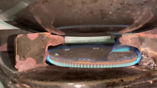 A close-up view of a gas stove burner with a blue flame igniting beneath a pot.