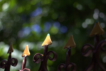Elegant metal fence with golden tips against blurred green background, creating serene atmosphere. intricate design adds touch of artistry to scene