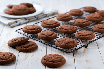 Tasty chocolate cookies are cooling after baking on a rack on a white table, selective focus.