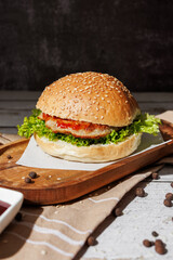 hamburger with green salad, tartar sauce, ketchup, sesame bun, on a dark background with sauces, fast food, snack