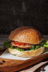 hamburger with green salad, tartar sauce, ketchup, sesame bun, on a dark background with sauces, fast food, snack