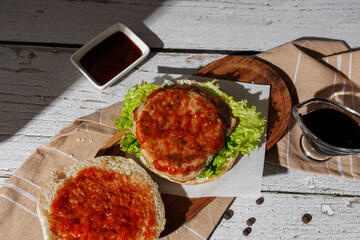 open hamburger with green salad, tartar sauce, ketchup, sesame bun, on a dark background with sauces, fast food, snack