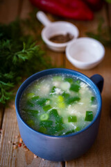 Home cooking: chicken soup with vegetables, fresh herbs and egg in a blue plate on a wooden table. Hot chicken soup for lunch. Vertical photo. Close-up.