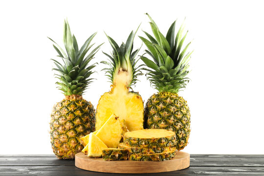 Whole and cut ripe pineapples on wooden table against white background