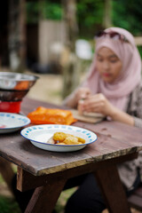 young Indonesian woman in hijab slicing sausages while camping in a forest cabin, travel concept.