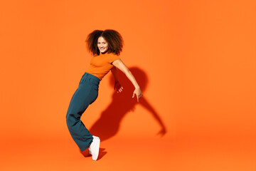 Afro woman standing on tiptoe in front of orange background