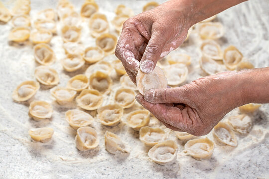 Chef cook hands making handmade Tortellini ravioli on table with flour. Closeup of the floured hands of the chef showing the ravioli just finished and ready to be cooked. Woman making meaty ravioli