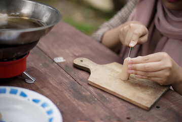 young Indonesian woman in hijab slicing sausages while camping in a forest cabin, travel concept.