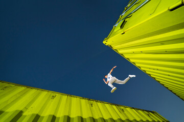 Man jumping over green cargo containers under blue sky