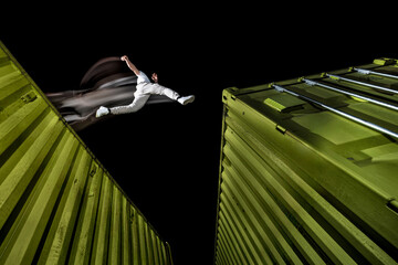Young man practicing free running over green cargo containers