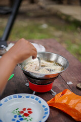 Man's hand frying sausages on portable stove while camping in forest cabin, travel concept.