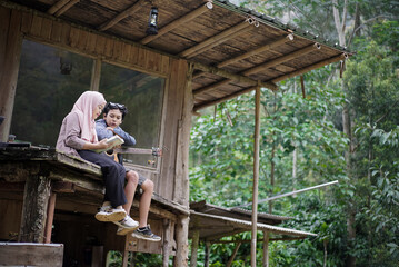 young Indonesian man and woman in hijab relaxing in a jungle cabin together while playing guitar and reading a book, travel concept.