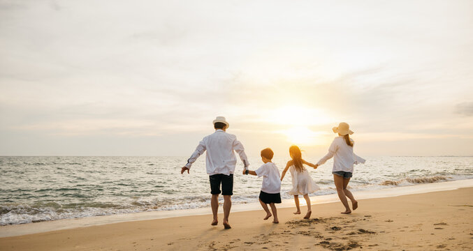 Asian family happiness at beach parents and daughters play together. Back view captures joyful moments of little girls bonding with their mother and father pretending to fly on carefree weekend.