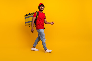 Cheerful courier in red t-shirt and hat carrying yellow bag, walking confidently against vibrant yellow background
