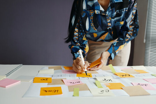 Medium section of unrecognizable woman standing at desk using sticky notes while planning work in modern office