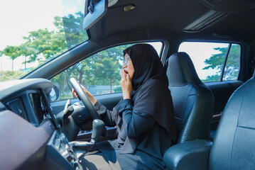 A woman in a black hijab is driving a car and appears to be in pain. She is shocked.