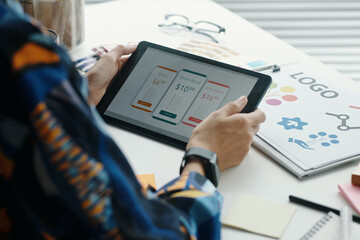 Over shoulder shot of unrecognizable woman holding digital tablet in hands and choosing...