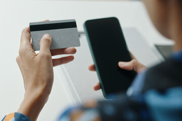 Over shoulder of unrecognizable young woman holding bank card buying goods online via smartphone app