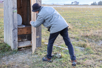 The countryman is in desperate need of using an old wooden outhouse (privy) in the countryside.