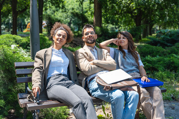 Group of young business people sitting on the bench outside office building in downtown district, talking discussing and resting till waiting the staff meeting and presentation of new project ideas.